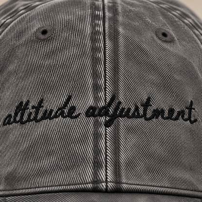 Close-up of a washed black baseball cap with 'altitude adjustment' embroidered in black script across the front.