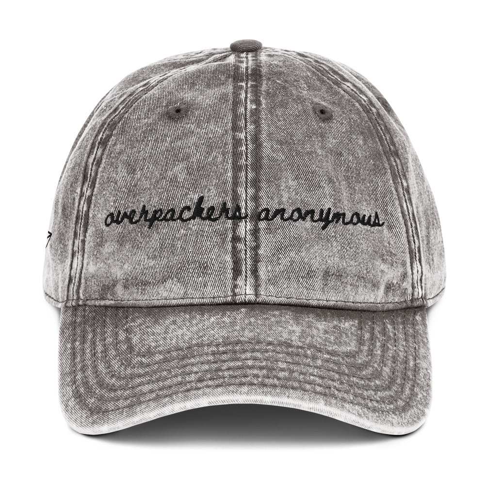 Grey travel themed vintage wash hat with words "overpackers anonymous" on it