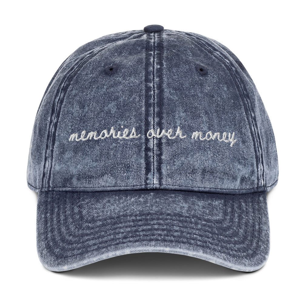 Vintage navy travel themed hat with the words "memories over money" embroidered on it